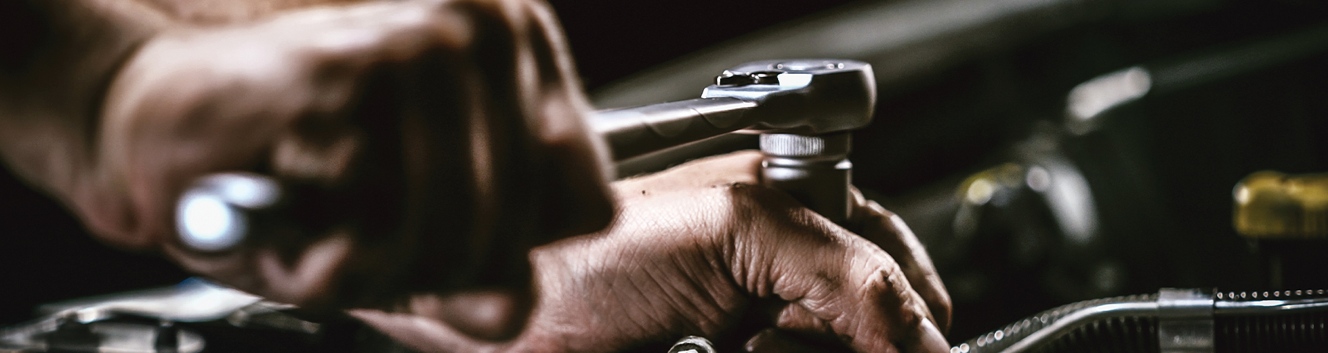 Close-up of a technician's hands holding a wrench and working on vehicle's engine.