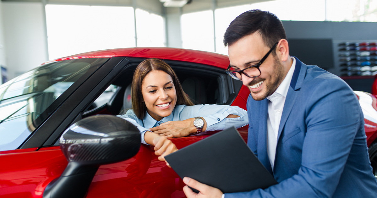 A car salesperson showing a customer sitting in a car at the dealership paperwork