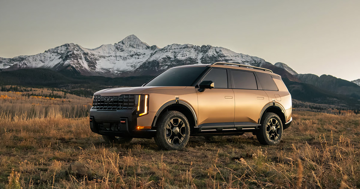A Kia Telluride parked in a field with a mountain visible in the background during sunset.